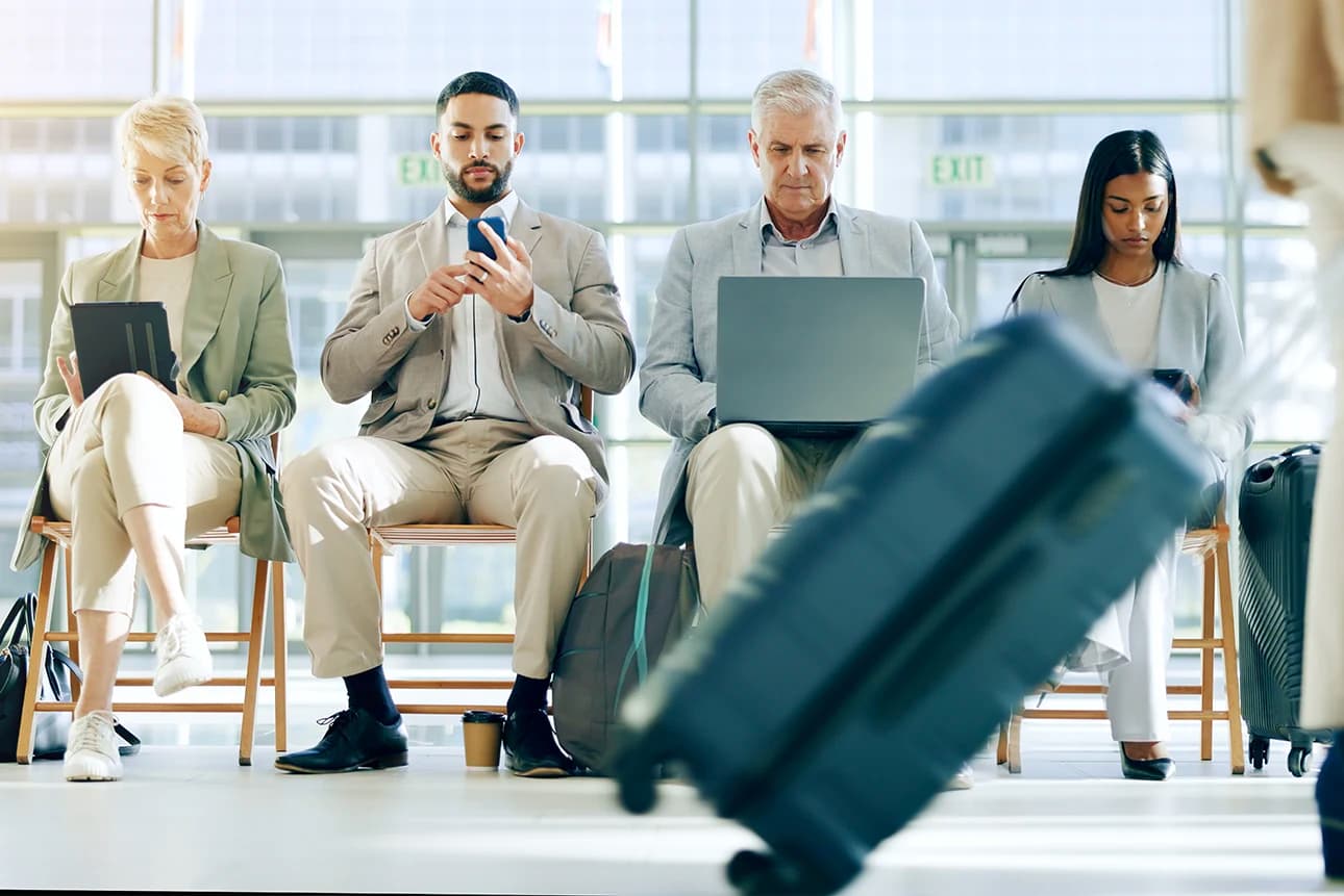Employees and businesspeople checking flight schedules and working on devices in an airport waiting room.