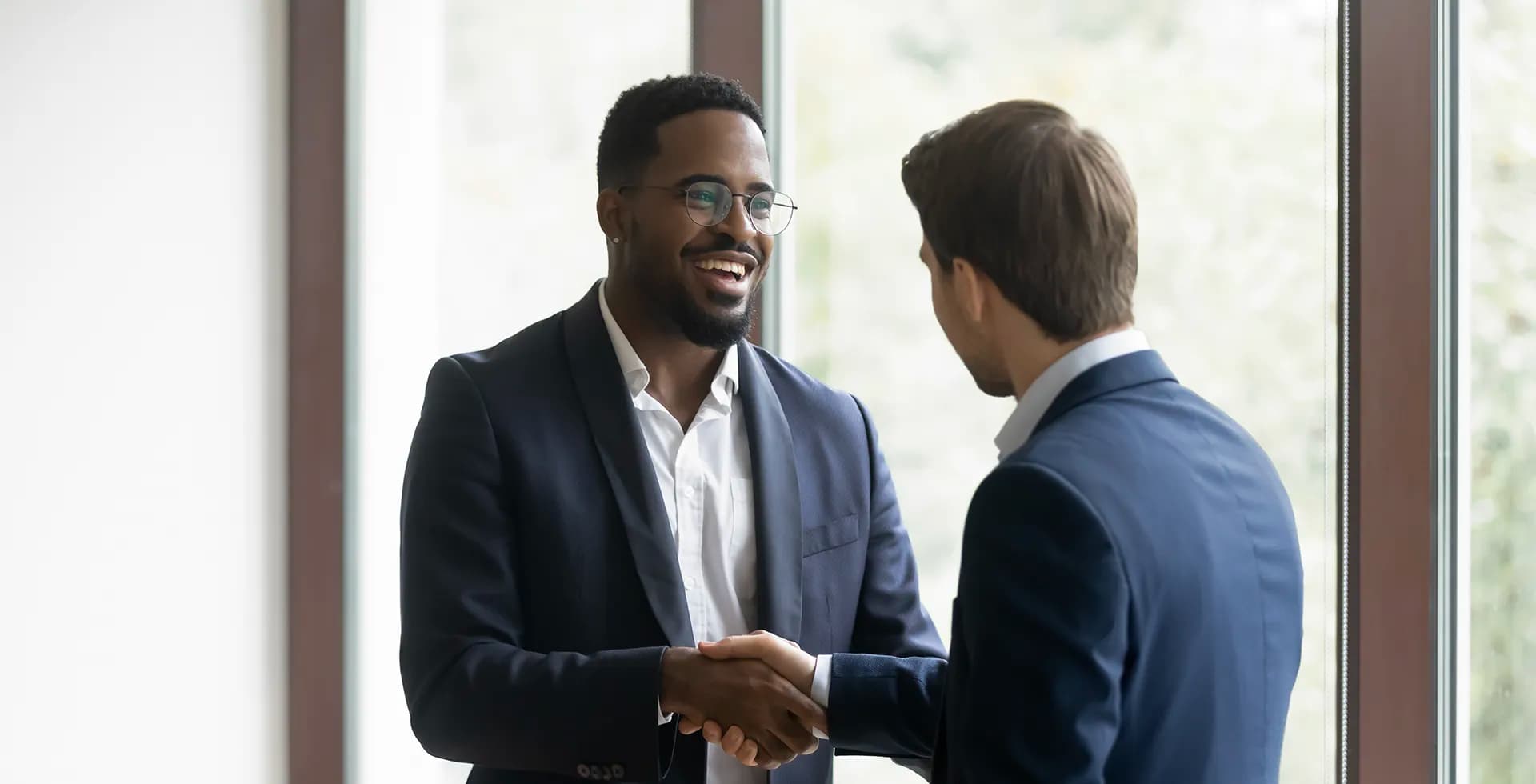 Overjoyed multiethnic businessmen shake hands greeting getting acquainted in office