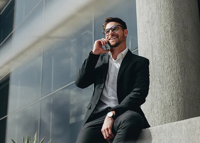Smiling business person taking on mobile phone sitting outdoors 